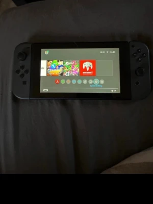 Nintendo Switch grå - Nintendo Switch spelkonsol med grå Joy-Con, perfekt för gaming både hemma och på språng. Konsolen har en stilren rektangulär design i plast och levereras med originalkartong, dockningsstation och tillbehör. En grym maskin för dig som älskar spel och flexibilitet.