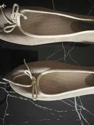 Beige ballerinaskor med rosett - Snygga beige ballerinaskor med rund tå och dekorativ rosett framtill. Skorna har en enkel och stilren design med textilmaterial och randigt innerfoder. Perfekta för en avslappnad och trendig look.