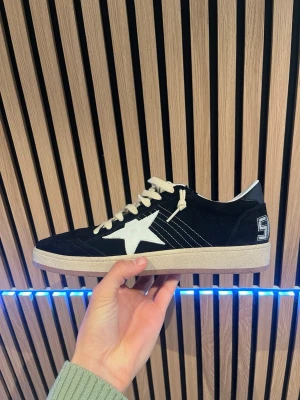 Golden goose ballstars skor - Svarta sneakers från Golden Goose med vit stjärndetalj på sidan, vita snören och vit sula. Skon har en broderad siffra på hälen och är tillverkad i mocka och läder. Klassisk låg modell med coola kontrastdetaljer och retrovibbar.
