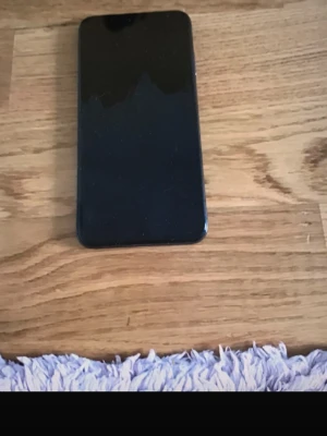 Svart iPhone XS Max  - Säljer en svart iPhone med stilren design och glasbaksida. Telefonen har rundade hörn och en slimmad form som känns modern och smidig i handen. Perfekt för dig som gillar Apple och vill ha en snygg mobil med klassisk look.