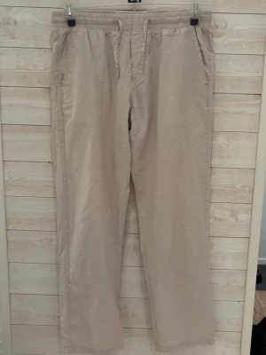 Beige linnebyxor med resårmidja - Snygga beige linnebyxor med avslappnad passform och resår i midjan. Byxorna har sidfickor och en bakficka, perfekta för en chill och stilren look. Lätta och luftiga, passar perfekt till varmare dagar.