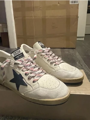 Golden goose Ballstars röd/blå - Säljer ett par ett par iprincip helt nya snygga sneakers från Golden Goose med blå stjärna på sidan och röda detaljer. Skorna har randiga snören i vitt och rött samt GGDB-logga på plösen. Ovandelen är i skinn med perforerade detaljer framtill och beige sula. Skorna har blivit minimalt använda. Box och dustbag tillkommer. Skriv vid fler funderingar 🙌