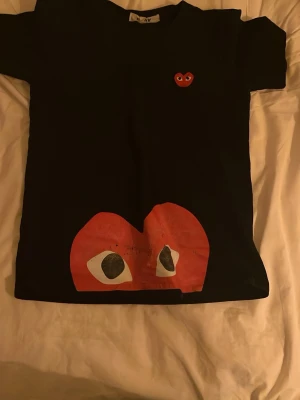 Svart Comme des Garçons Play t-shirt - Svart t-shirt från Comme des Garçons Play med det ikoniska röda hjärta-trycket med ögon framtill och ett mindre hjärta på bröstet. Klassisk passform och rund hals. Perfekt för dig som gillar streetwear och vill sticka ut.Tyvär rätt dåligt skick.Priset är Inte fast hugget.