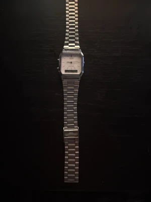 Casio silverfärgad armbandsklocka - Stilren armbandsklocka från Casio med rektangulär urtavla i vitt och digital display. Klockan har en klassisk länk i silverfärgat metall och minimalistisk design. Perfekt accessoar för dig som gillar retrostil och funktionalitet.