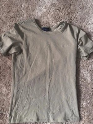 Beige t-shirt från GANT - Snygg beige t-shirt från GANT med diskret logga broderad på bröstet. Klassisk rund halsringning och korta ärmar. Tillverkad i mjuk bomull som känns skön mot huden. Perfekt basplagg för en clean och enkel stil. Passar även M!