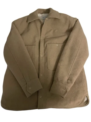 Beige overshirt från Weekday - Stilren beige overshirt från Weekday i mjukt ull-liknande material. Modellen har två stora bröstfickor, knäppning framtill och klassisk krage. Perfekt lager-på-lager-plagg med avslappnad passform och långa ärmar.