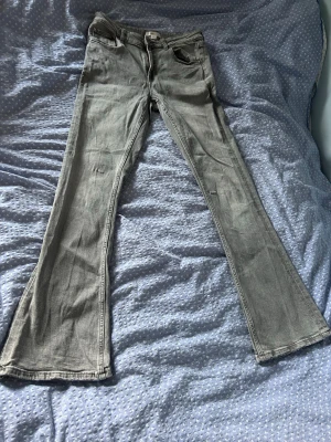 Grå bootcut jeans med utsvängda ben - Säljer ett par gråa bootcut jeans med utsvängda ben och klassisk femficksdesign från Gina young . Storlek 164 men passar mig som brukar ha storlek 34 i jeans. Jeansen har normal midja och dragkedja med knapp framtill. Materialet är denim i bomullsmix och färgen är en snygg tvättad grå nyans.