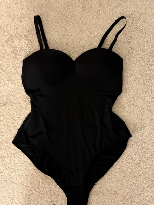 Svart body  - Snygg svart body som är kroppsformad. Bodyn är super bekväm! Inte i string men tyget är inte synligt genom byxorna.  Helt ny säljer pga köpt i fel storlek! 