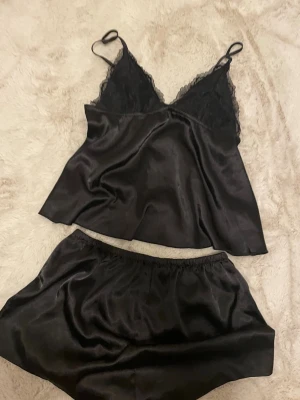 Svart satinset med spetsdetaljer - Ett svart set i satin med linne och shorts. Inte använt!