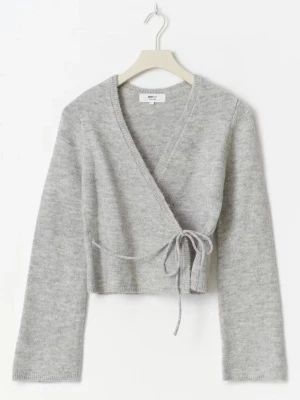 Grå omlottkofta från gina tricot - Mjuk och stilren grå omlottkofta från Gina Tricot med knytband i sidan. Koftan har lång ärm och är tillverkad i ett fluffigt stickat material. Helt oanvänd.