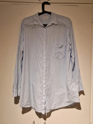 Ljusblå randig skjorta med ficka från Filippa K - Klassisk snygg skjorta från Filippa K med tunna blåa ränder. Skjortan har lång ärm, bröstficka och knappar framtill. Tillverkad i mjuk bomull för en avslappnad och bekväm känsla.