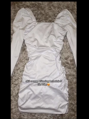 Vit puffärm klänning med rynk - Trendig vit klänning med långa puffärmar och rynkdetaljer framtill och på sidorna. Klänningen har en fyrkantig urringning och är figurnära i modellen. Perfekt för dig som vill sticka ut med en modern och stilren look.