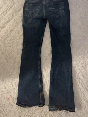  bootcut jeans  - Säljer ett par klassiska blå bootcut jeans från Wrangler med ikoniska kontrastsömmar på bakfickorna och läderpatch i midjan. Jeansen har normalhög midja och är tillverkade i slitstark denim. Perfekta för en avslappnad och tidlös stil.