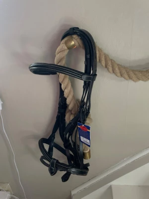 Svart träns från Knights i läder - Säljer ett svart träns från Knights i strl full, tillverkat i mjukt och följsamt läder. Tyglar med följer. Tränset har eleganta sömmar och detaljer i mässing. Passar till häst och är perfekt för både tävling och vardagsridning. Köpte tränset för 700kr. Märket står för hög kvalitet och snygg design. Helt nytt från butik. Skriv om du har några frågor!