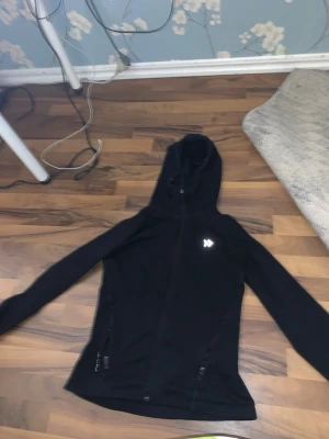 Svart hoodie från lager 157 - Snygg svart hoodie från lager 157 med dragkedja framtill och två fickor med dragkedja. Hoodien har en klassisk huva och en liten logga på bröstet. Perfekt för en avslappnad och sportig stil.
