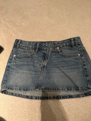 Blå jeanskjol i klassisk modell - Säljer en blå jeanskjol i kort modell.  Kjolen har en klassisk denimlook och är perfekt för dig som gillar en enkel och tidlös stil.