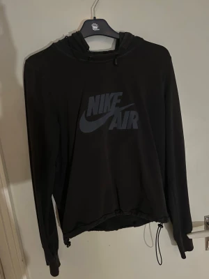 Svart Nike Air hoodie med huva - Säljer en svart hoodie från Nike Air med stor logga på bröstet. Hoodien har justerbar huva med snören och ribbade muddar vid ärmsluten. Materialet känns mjukt och bekvämt, perfekt för en avslappnad streetwear-look.
