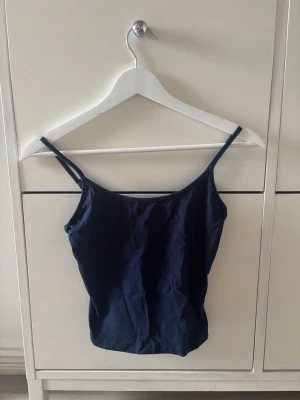 Mörkblå linnetopp med smala band - En enkel och stilren mörkblå linnetopp med smala axelband. Toppen har en rak passform och är tillverkad i mjukt bomullsmaterial, perfekt för varma dagar eller som lager under andra plagg. Använd fåtal gånger💕