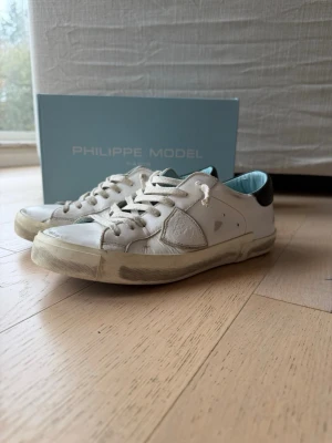 Vita Philippe Model sneakers  - Snygga vita sneakers från Philippe Model. Skorna har vita snören, ljusblå insida och svart detalj på hälen. Klassisk och en timeless sko som funkar för de mesta outfitsen. Priset är inte hugget i sten, fråga vilka frågor som helst och om du köper vid full pris får du dustbag också. Box och snören ingår i köpet ✌️🔥