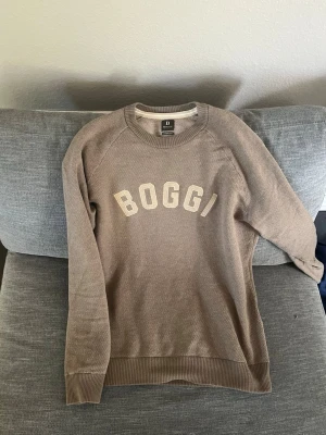 Kashmir tröja  från Boggi Milano - Snygg beige sweatshirt från Boggi Milano med tryckt logga på bröstet. Tröjan har rund halsringning, ribbade muddar och är tillverkad i mjukt material. Perfekt för en avslappnad och stilren look.
