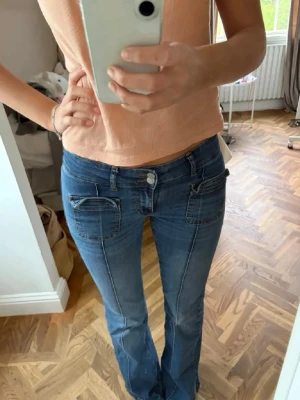 Blå bootcut jeans från Nelly - Snygga blå bootcut jeans från Nelly med dubbla knappar i midjan och stora fickor framtill. Jeansen har markerade sömmar och en klassisk denimlook som passar perfekt till en trendig vardagsstil.