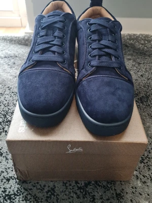 Mörkblå mockasneakers Salvatore Ferragamo - Snygga mörkblå sneakers i mocka från Salvatore Ferragamo. Skorna har klassisk låg profil, matchande blå snörning och ikonisk röd sula med Ferragamo-logga. Insidan är fodrad i beige läder för extra komfort. Perfekta för dig som vill ha stilrena och exklusiva sneakers.
