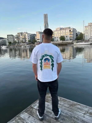 Vit Casablanca t-shirt med tryck - Snygg vit t-shirt från Casablanca med färgglatt tryck på ryggen och mindre tryck på bröstet. T-shirten har normal passform, korta ärmar och är gjord i mjuk bomull. Perfekt för dig som vill sticka ut med en unik design och fräscha färger.