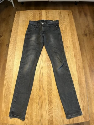 Grå slim fit jeans från Replay - Säljer ett par grå slim fit jeans från Replay med klassisk femficksmodell och diskreta slitningar. Jeansen har normal midja, smala ben och är tillverkade i mjuk denim med stretch för extra komfort. Perfekta för en avslappnad och trendig look.