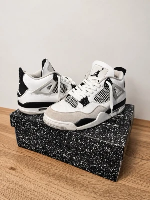 Air Jordan 4 Military Black - Säljer ett par Air Jordan 4 ”military black” i. Skorna har klassisk meshpanel, mockadetaljer och ikoniska Jumpman-loggan på plösen. Snygg kontrast mellan färgerna och cool retrovibe. Perfekta för dig som gillar streetwear och sneakerskultur.