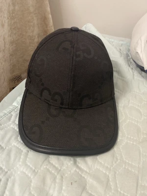 Svart keps från Gucci med GG-mönster - Snygg svart keps från Gucci med klassiskt GG-monogram över hela kepsen. Kepsen har böjd skärm med läderkant och justerbar rem bak. Tillverkad i textilmaterial med exklusiv känsla, perfekt för dig som vill sticka ut med en lyxig accessoar.