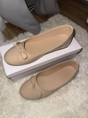 Beige ballerinaskor med rosett - Säljer ett par stilrena beige ballerinaskor från NELLY. Skorna har rund tå, dekorativ rosett framtill och är tillverkade i ett slätt material med diskret glans. Perfekta för dig som gillar en enkel men chic look.