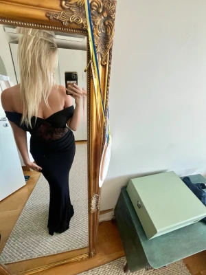 Svart långklänning med spetsdetaljer - Svart långklänning med offshoulder-modell och transparenta spetsdetaljer över midjan. Klänningen är endast testad, köpt från Australien och betalade tull. Står storleken 40 men skulle säga att den passar 38/36 bättre.