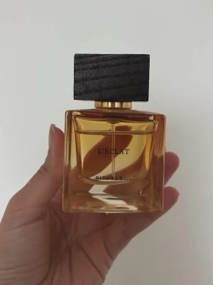Rituals L'Éclat parfym - Snygg parfymflaska från Rituals med namnet L'Éclat. Flaskan är fyrkantig i glas med guldiga detaljer och har en stilren, mörk träkork. Perfekt som en lyxig detalj på sminkbordet. 40/50 ml kvar. Ordpris 619 kr