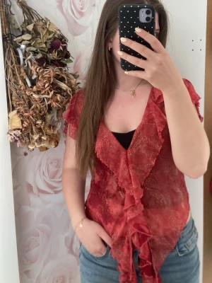 Röd volangblus med paisleymönster - Snygg omsydd röd blus med volangkant och paisleymönster. Blusen är genomskinlig och har korta ärmar samt djup v-ringning med volanger längs kanten❣️