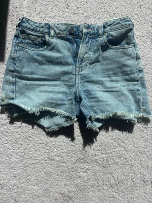 Ljusblå jeansshorts Scotch & Soda - Säljer ett par ljusblå jeansshorts från Scotch & Soda med fransiga benslut och klassisk femficksmodell. Shortsen har knappgylf och bälteshällor, perfekta för sommardagar. Snygg, avslappnad passform och mjukt denimtyg. Som en 32 i strlk. Men egentligen 14 år