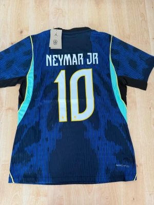 Neymar Jr #10 – Player Edition Brasilien (storlek M) - Neymar Jr #10-tryck. Player Edition Brasilien. Storlek M. Helt ny och aldrig använd. Säljs i befintligt skick. Skickas snabbt! 🚚💨  Mått för denna tröja (storlek M): (Uppmätta av leverantör – viss variation kan förekomma) • Halva bröstmåttet: 51 cm • Tröjans längd: 72,5 cm • Ärmbredd: 22,5 cm • Axelbredd: 43 cm • Ärmlängd: 39 cm • Manschettbredd: 18 cm  🔥 Player Edition-modell – tajtare passform än vanliga supportertröjor. 🇧🇷 Brasilien landslag.