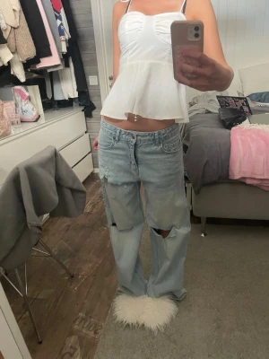 Baggy ljusblå ripped jeans - Baggy ljusblå jeans med stora hål på knäna och lös passform. Jeansen har klassisk femficksdesign och är tillverkade i denim. Perfekta för en avslappnad och trendig streetstyle-look.