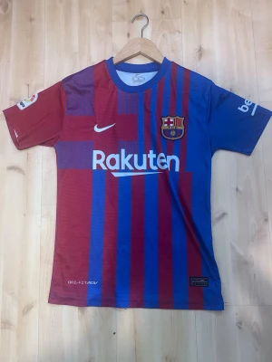 FC Barcelona matchtröja Nike - Säljer en officiell FC Barcelona matchtröja från Nike med klassiska blå och vinröda ränder. Tröjan har klubbmärke, sponsorloggor och La Liga-märke på ärmen. Tillverkad i lätt och ventilerande material, perfekt för fotbollsträning eller att bära på läktaren.