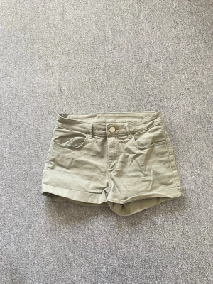 Gröna shorts med fickor och knapp - Snygga gröna shorts med klassisk femficksdesign, knapp och dragkedja framtill samt uppvikta benslut. Perfekta för varma dagar och enkla att matcha med olika toppar.