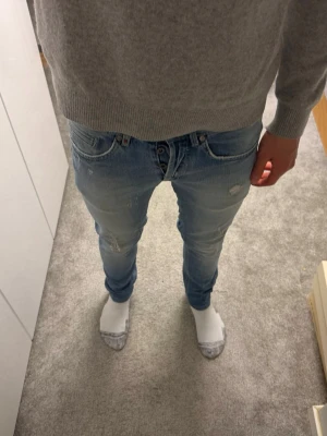 Lite schysstare DonDups  - Säljer ett par ljusblå slim fit jeans med snygga slitningar och tvättade detaljer. Jeansen har klassisk femficksdesign och knäppning fram. Perfekta för en avslappnad och trendig look.