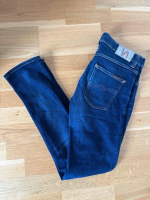 Mörkblå jeans från Nudie Jeans - Säljer ett par Nudie Jeans, Grim Tim. Passformen är slim och har lite stretch. Endast använda 1-2 gånger så utmärkt skick. Storlek 30/32