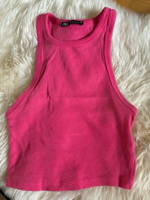 Rosa ribbad linnetopp från Zara - Snygg rosa ribbad linnetopp från Zara. Toppen är ärmlös med rund halsringning och croppad passform, perfekt för en trendig look. Materialet är mjukt och stretchigt för extra komfort.