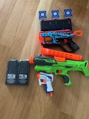 Leksakspistoler och tillbehör X-Shot perfekt present till ditt barn  - Säljer ett paket med tre färgglada leksakspistoler från X-Shot, inklusive magasin, måltavlor och tillbehör. Pistolerna är i plast och har detaljer i blått, grönt, orange, vitt och svart. Perfekt för roliga skjutlekar och tävlingar med vänner.