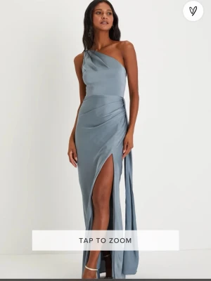 Perfekt balklänning Ljusblå långklänning med slits - Snygg ljusblå långklänning med oneshoulder och smala axelband. Klänningen har en elegant slits framtill och är figurnära med en mjuk, glansig finish. Perfekt för dig som vill sticka ut med en stilren look.