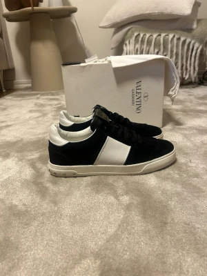Valentino Flycrews skor - Brand new allt og (dustbag - box - etikett- extra spik) Snygga svarta sneakers från Valentino Garavani med vit panel på sidan och vita detaljer vid häl och sula. Skorna har svarta skosnören, klassisk låg modell och små nitar på sulan. Materialet är en mix av mocka och läder för en lyxig känsla.