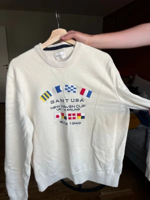 Vit långärmad sweatshirt från Gant - Vit sweatshirt från Gant med broderade flaggor och text på bröstet. Herrmodell i strl L! Knappt använd och mycket fint skick!