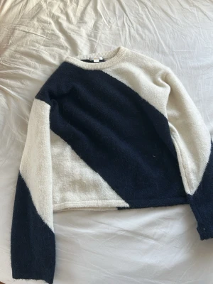 marinblå och vit stickad tröja med diagonal design - Snygg stickad tröja i marinblå och vitt med cool diagonal färgblock-design. Tröjan har rund halsringning och långa ärmar. Perfekt för dig som gillar en stilren men ändå unik look.