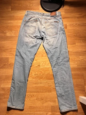 Nudie jeans ”Grim trim” W33 L34 Ljusblåa  - Authentic Nudie Jeans Grim Tim jeans in a clean light blue wash. Slim straight fit with natural fading — classic everyday pair.  * Size: W33 L34 * Fit: Grim Tim (slim straight) * Condition: Good – nicely worn in, no major flaws * Color: Light blue wash * Premium organic cotton denim * Signature Nudie stitching + leather patch