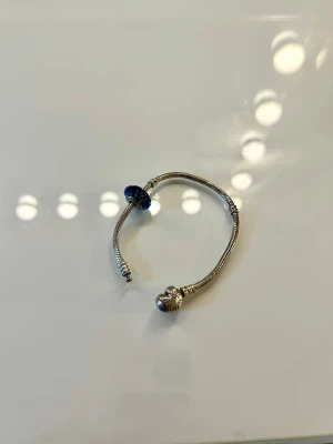 Pandora silverarmband med blå berlock - Säljer ett klassiskt Pandora armband i silver med en vacker glitter blå berlock. 🌌 Armbandet har den ikoniska runda låset med Pandora-loggan. Perfekt för dig som gillar att samla berlocker och vill ha någon stans att börja.💙💍
