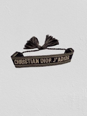 Dior armband - Christian Dior J'Adior ArmbandKlassiskt vävt armband i svart och vit. Skick: Bra begagnat skick. Notera: Lite av bokstaven ”R” i Dior har nötts bort (se bild). Detalj: Justerbar storlek med tofsar. Passar perfekt som en stilren accessoar!